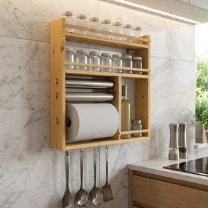 Könnte beinhalten: Ein wandmontierter Küchenorganizer aus hellem Holz mit zwei oberen Regalen für zwölf klare Glasbehälter, einem Mittelteil mit zwei Metallfolienrollen und einer Küchenrolle, einem Seitenfach für eine Flasche und vier Metallhaken mit Utensilien.