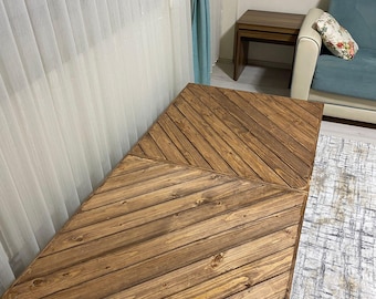 May include: A rectangular wooden coffee table with a chevron pattern. The table is made of light brown wood and has a rope handle on one side. The table is approximately 40 inches long and 20 inches wide.