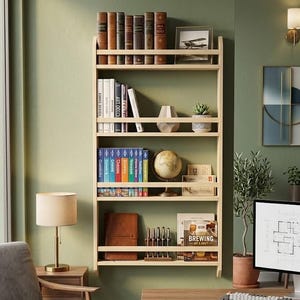 May include: A light-colored wooden wall-mounted bookshelf with four tiers, featuring protective rails on each shelf. The shelves are filled with various books, a small globe, a potted succulent, a framed picture, and a book titled Brewing.