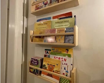 May include: Three wooden shelves mounted on a white wall, each shelf holds a variety of colorful children's books. The books have titles in both English and Turkish.