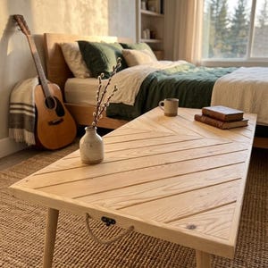 Pode incluir: Uma mesa de centro retangular de madeira clara com um tampo de padrão espinha de peixe, quatro pernas cónicas e uma pega de corda grossa fixada na lateral com um suporte de metal preto. A superfície apresenta um grão de madeira natural e clara.