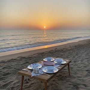 May include: A wooden picnic table set on a sandy beach, with a sunset over the ocean in the background. The table is set with white plates, bowls, silverware, and salt and pepper shakers. A pink serving dish is in the center.