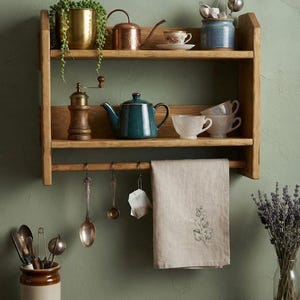 Peut inclure: Une étagère murale en bois à deux niveaux avec une jardinière en laiton, un arrosoir en cuivre, une théière bleu sarcelle, des tasses en céramique, un moulin à poivre en bois, un torchon en lin suspendu et diverses cuillères en métal.