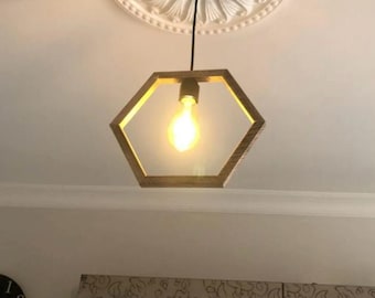 May include: A hexagonal wooden pendant light fixture with a single light bulb hanging from a black cord. The light fixture is suspended from a white ceiling medallion with a decorative floral design.