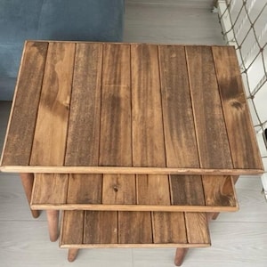 Może przedstawiać: Zestaw trzech drewnianych stolików wkładanych w siebie z naturalnym brązowym wykończeniem. Stoliki wykonane są z drewnianych desek i mają prosty, rustykalny design.