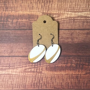 May include: A pair of white and gold rugby ball shaped earrings with silver hooks.