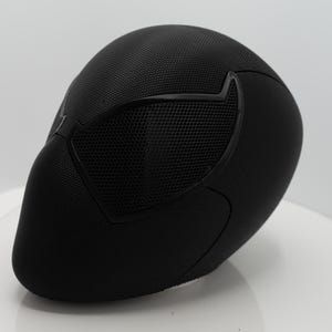 May include: A black mask with a textured surface and mesh eye covering. The mask has a streamlined design, with a smooth, curved shape. The eye covering is a darker black, creating contrast. Likely for cosplay or costume purposes.