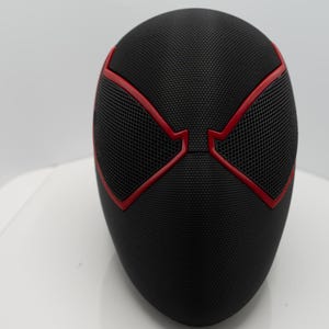 May include: A black mask with red detailing, with a mesh pattern over the eye areas. The mask has a smooth, curved form and is likely a costume or cosplay item.
