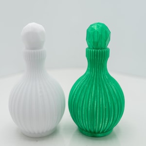 May include: Two decorative bottles, one white and one green, with ribbed bodies and faceted stoppers. The bottles have a bulbous shape and a narrow neck. The green bottle has a vibrant color, while the white bottle is a neutral tone.
