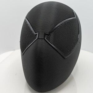 May include: A black mask with a textured surface and mesh eye coverings. The mask has a distinct design with angular shapes around the eyes, and is likely a costume or cosplay accessory.