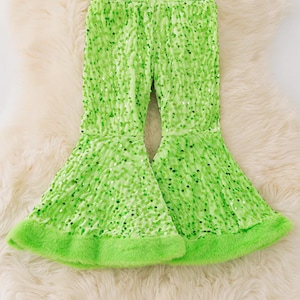 May include: Lime green sequin trousers with a flared leg design. The trousers have a soft, fluffy trim at the bottom of the flared legs and a matching green elastic waistband. The trousers are displayed on a fluffy, white surface.