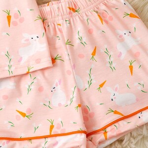 Peut inclure: Ensemble de pyjama rose avec un motif de lapins blancs, de carottes oranges et de brins verts. Le short et le haut ont une bordure orange. Le tissu est doux et l&eacute;ger, parfait pour le printemps ou P&acirc;ques.