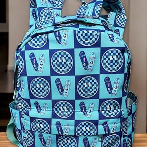 May include: A blue and navy checkered backpack with a smiley face and skateboard pattern.