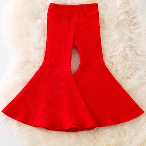 May include: Bright red, ribbed knit trousers with a flared leg design. The trousers are made of a soft material and are suitable for everyday wear. The trousers are shown on a white, fluffy surface.