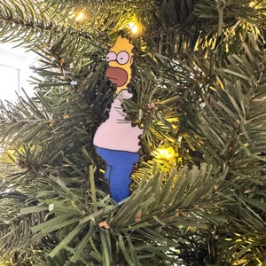 Adorno navideño con el meme gracioso de Homero Simpson en el arbusto