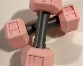 May include: A pair of pink 1 lb dumbbells with gray handles. The dumbbells are made of a textured material and have the number "1" embossed on each side.