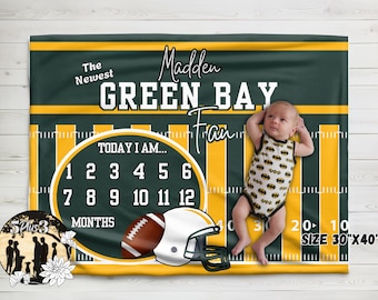 Puede incluir: Una manta de hitos rectangular con diseño de campo de fútbol americano verde y amarillo, el texto The Newest Madden Green Bay Fan y un rastreador circular de 1 a 12 meses con un casco de fútbol, que mide 76 cm por 102 cm.