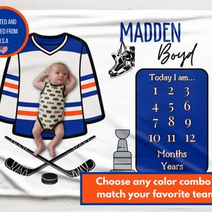 May include: A white baby blanket with a hockey theme, featuring a jersey design, hockey sticks, and a baby. The blanket includes the name "MADDEN Boyd" and a milestone tracker. The text "Choose any color combo to match your favorite team!" is also included.