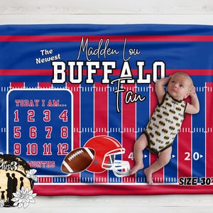 May include: A rectangular milestone blanket featuring a blue and red striped football field design. Text reads The Newest Madden Lou BUFFALO Fan and TODAY I AM 1-12 MONTHS. Includes a football, helmet, and a 30 inch by 40 inch size label.