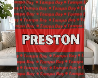 May include: A personalized blanket featuring the name "PRESTON" in large white letters on a red stripe. The blanket has a gray background with the words "Tampa Bay" and red dots repeated throughout. A cozy, custom gift.