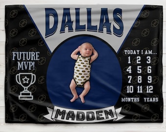 Op de afbeelding: Een zwart-witte babydeken met een voetbalthema. Het heeft een babyfoto, de woorden "Dallas Madden", "Future MVP!" en een nummertabel om de groei van een baby bij te houden. De deken heeft een blauw-wit kleurenschema met gouden accenten.