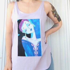 May include: A lavender tank top with a graphic print of a woman with blue and purple hair, wearing large gold earrings. The woman is looking down and has a blue background.
