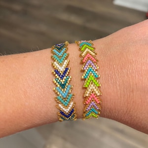Puede incluir: Dos pulseras de cuentas con patrones de chevrón. Una pulsera presenta una combinación de colores turquesa, blanco, azul marino y dorado. La otra pulsera tiene una combinación de colores rosa, verde, morado y dorado. Las pulseras están hechas de pequeñas cuentas.