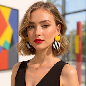 Puede incluir: Una mujer con pendientes geométricos llamativos. Los pendientes presentan una parte superior cuadrada amarilla y un círculo a rayas blancas y negras. Lleva pintalabios rojo y una camiseta negra. El fondo incluye obras de arte coloridas y una ventana.