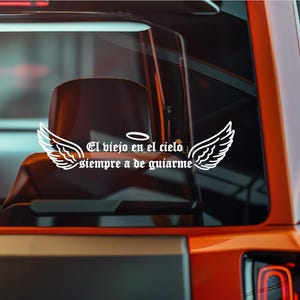 May include: White vinyl decal featuring angel wings and the text "El viejo en el cielo siempre a de guiarme." The decal is designed to be applied to a car window or similar surface. The text is in a stylized font.