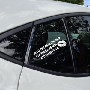 May include: White car window decal with the text "SI LO VEN ESTA CASADO Y LA TROCA ES MIA ATT: SU ESPOSA" and a white lip print. The decal is applied to the rear window of a white car.