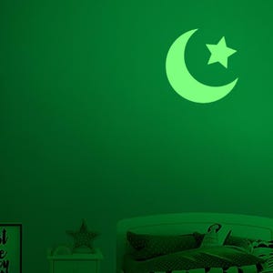 May include: A glowing green crescent moon and star wall decal on a green wall. The celestial shapes are a soft, luminous green, creating a calming ambiance. The decal is likely for a child's bedroom.