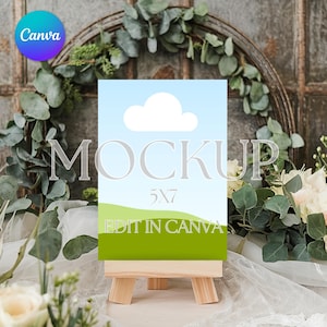 May include: A 5x7 inch blank canvas mockup on a wooden easel with a green and blue background. The canvas is set against a backdrop of greenery and white fabric.