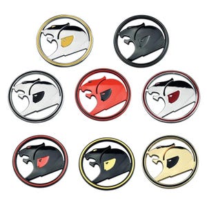 May include: Set of ten round car badges featuring a stylised animal head design. The badges are in various colour combinations, including black, white, red, gold, and silver.