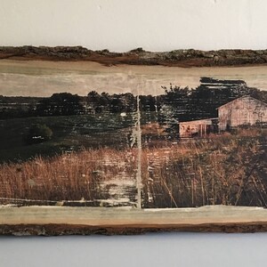 May include: A rustic wooden sign with a printed image of a farmhouse in a field. The sign has a natural wood grain and a distressed finish.