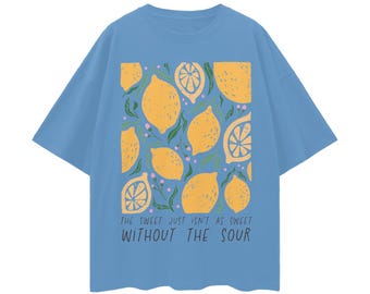 May include: A light blue t-shirt featuring a pattern of yellow lemons and green leaves. The text "THE SWEET JUST ISN'T AS SWEET WITHOUT THE SOUR" is printed in black. The shirt has short sleeves and a crew neck.