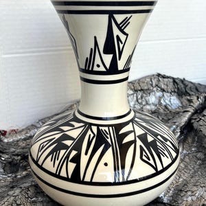 Puede incluir: Una taza de cerámica blanca con un asa negra y el texto "But First, Coffee" en negro, con una fuente de estilo manuscrito. La taza está sobre una superficie blanca.