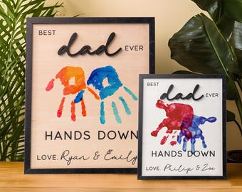 Peut inclure: Deux panneaux en bois encadrés avec des empreintes de mains et le texte "Best dad ever" et "Hands Down". Le premier panneau a des empreintes de mains bleues et orange et le texte "Love. Ryan & Emily". Le deuxième panneau a des empreintes de mains rouges et bleues et le texte "Love. Philip & Zoe".