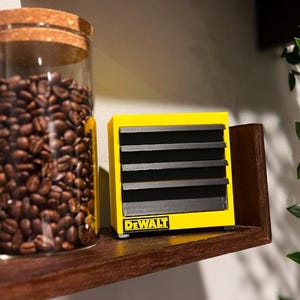 May include: A yellow and black miniature DeWalt heater on a wooden shelf with a glass jar filled with coffee beans.