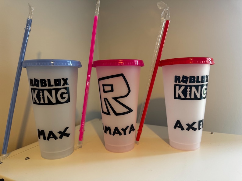 Reusable plastic cups with lids and straws. The cups are decorated with the words "Roblox King" and names.
