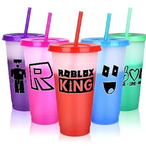 Set of  colourful reusable tumblers with lids and straws. Each tumbler features a different design, including a Roblox King logo, a smiley face, and a peace sign with a heart.