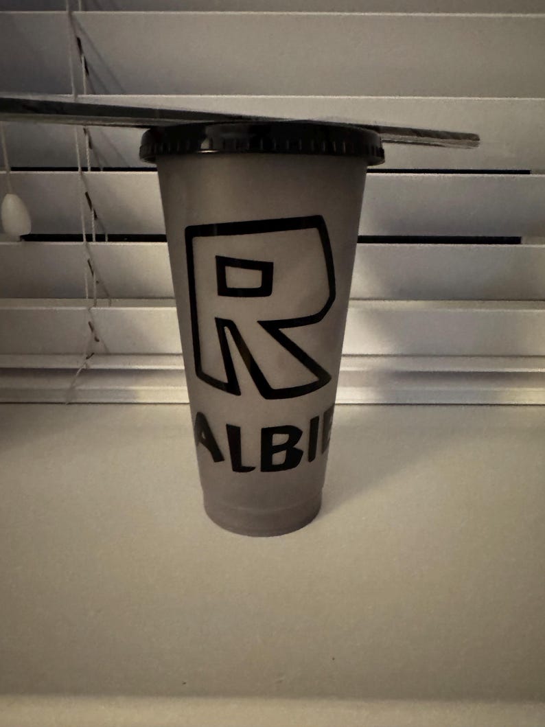 Puede incluir: Un vaso reutilizable gris con una letra "R" negra y la palabra "ALBI" impresa en &eacute;l.