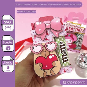 May include: A pink and white cardboard box with a cut-out window to display a mini M&M's tube. The box features a pink bow, a cartoon character with heart-shaped glasses, and the text "Happy Valentines".