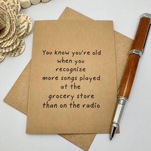 May include: A brown card with the text "You know you're old when you recognize more songs played at the grocery store than on the radio".