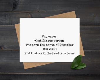 May include: A white greeting card with black text that reads "Who cares what famous person was born the month of December YOU WERE and that's all that matters to me." The card is on a brown envelope, with two green leaves.
