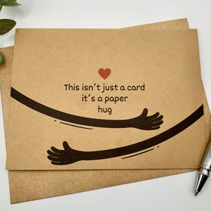 May include: A brown card with a red heart and black arms forming a hug. The card reads "This isn't just a card it's a paper hug".