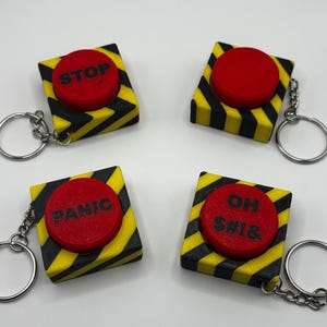 May include: Four red button keychains with black and yellow striped frames. The buttons have the words "STOP", "PANIC", "OH", and "SH*T" printed on them.
