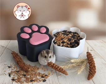 May include: A small hamster eats a piece of millet next to a black paw-shaped container with pink pads and a white paw-shaped bowl filled with mixed seeds. A circular logo featuring a cartoon hamster is visible in the upper left corner.