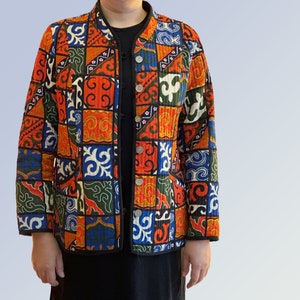 Op de afbeelding: Een kleurrijk gewatteerd jack met een patchwork-ontwerp met geometrische patronen in tinten rood, blauw, groen en wit.