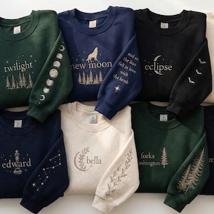 May include: A selection of crew neck sweatshirts in different colours, each embroidered with designs and text. The designs include phrases such as "twilight", "new moon", and "eclipse", along with illustrations of trees, moons, and constellations.