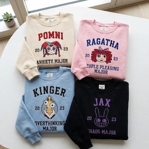Op de afbeelding: Vier sweaters met ronde hals in beige, roze, lichtblauw en zwart. Elk heeft een karakterafbeelding met de naam Pomni, Ragatha, Kinger of Jax, het jaar 20 23 en een hoofdtitel: Anxiety, People Pleasing, Overthinking of Chaos Major.